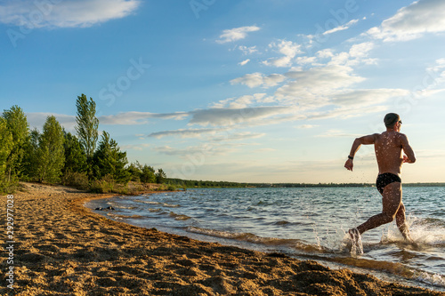 Athlete running into a lake at summer sunset for swim training 
