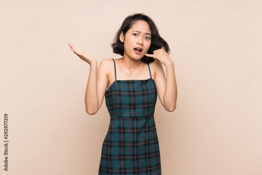 Asian young woman over isolated yellow wall making phone gesture and doubting Asian young woman over isolated yellow wall making phone gesture and doubting