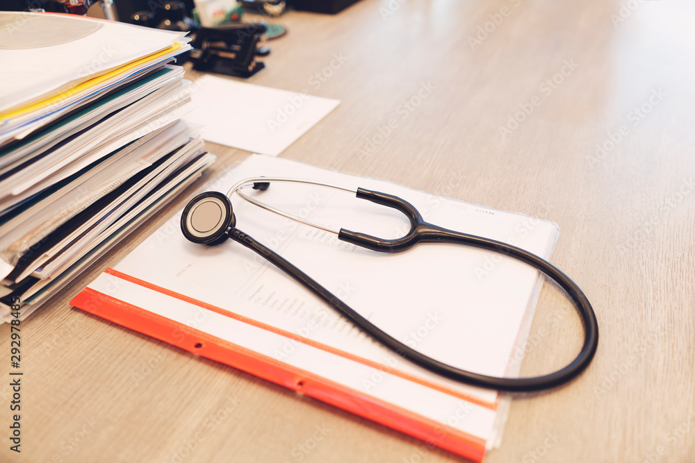 Stethoscope with black medical clipboard on wooden desk Stethoscope with black medical clipboard on wooden desk