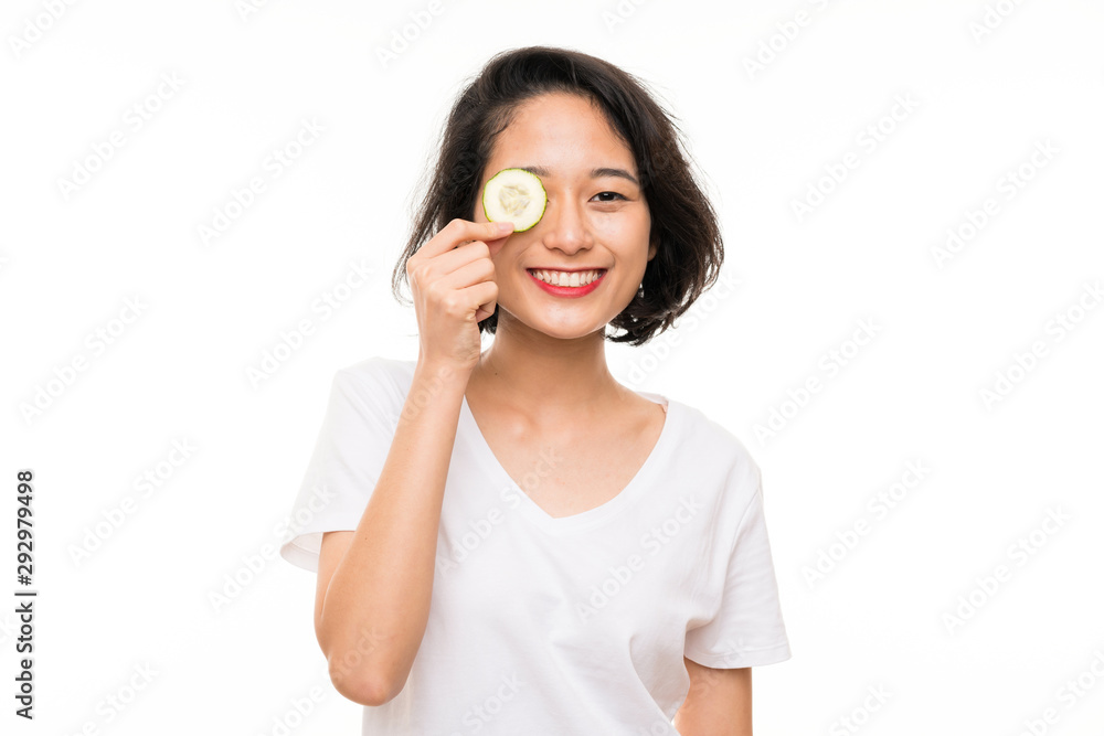 Asian young woman over isolated background holding slices of cucumber Asian young woman over isolated background holding slices of cucumber