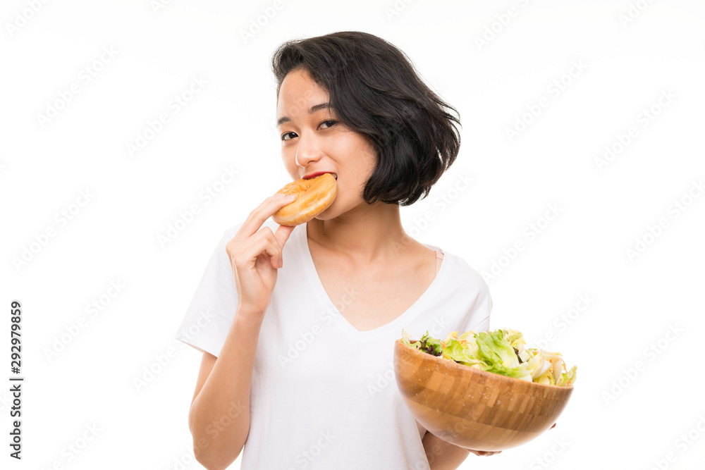 Asian young woman over isolated background with salad and donut Asian young woman over isolated background with salad and donut