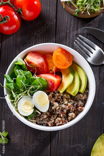 Fresh healthy salad with quinoa, cherry tomatoes and mixed greens, avocado, egg and micro greens on wood background top view. Food and health. Superfood meal. Clean eating. Healthy lifestyle