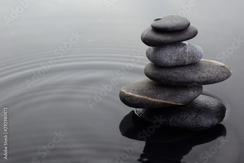 Zen stones in balanced pile in water on rippled water surface.