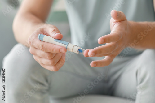 Diabetic man taking blood sample with lancet pen at home  closeup