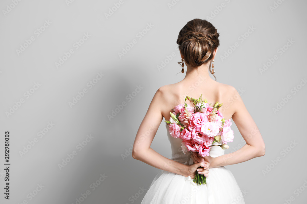 Beautiful young bride with wedding bouquet on grey background, back view Beautiful young bride with wedding bouquet on grey background, back view