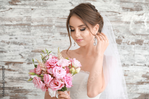 Portrait of beautiful young bride with wedding bouquet on wooden background
