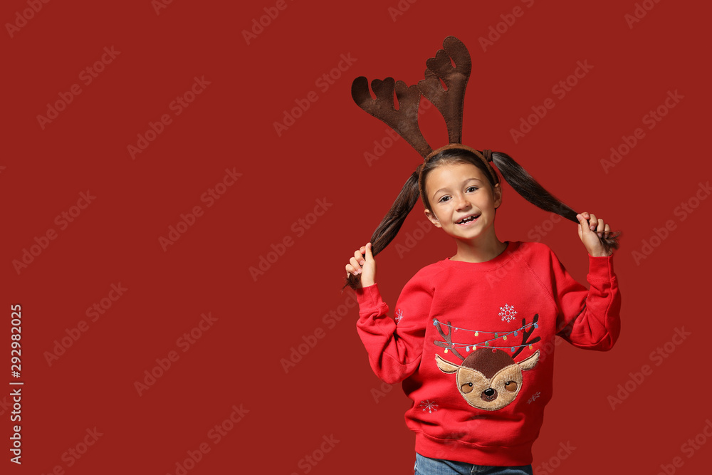 Cute girl in Christmas sweater and with deer horns on color background Cute girl in Christmas sweater and with deer horns on color background