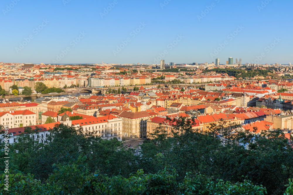 Panoramic view over the roofs and historical buildings of Prague the capital of the Czech Republic in a sunny day with trees and shrubs in the foreground