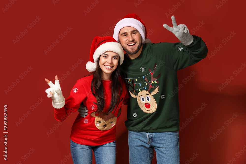 Fototapeta premium Young couple in Christmas sweaters and Santa hats on color background