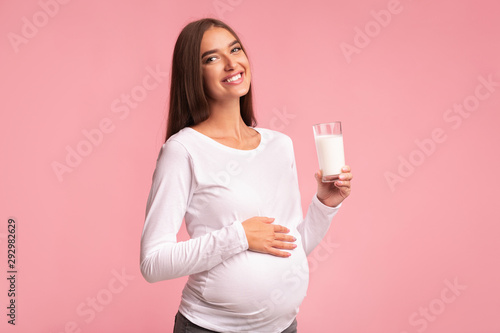 Fotografie Pregnant Woman Holding Glass Of Milk Standing Over Pink Background