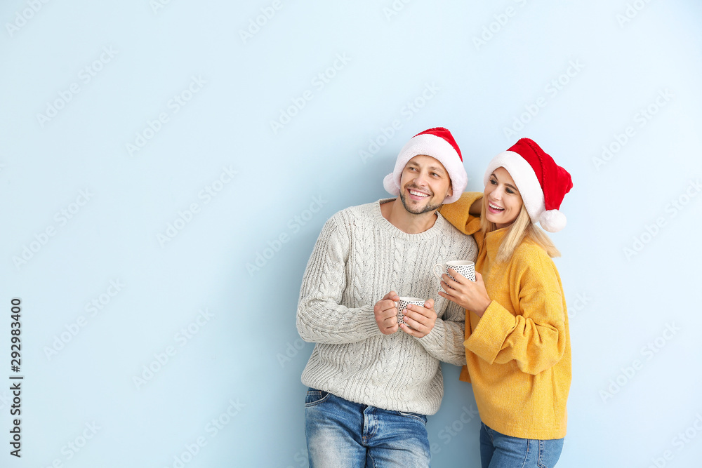 Happy couple in Santa hats drinking hot chocolate on color background Happy couple in Santa hats drinking hot chocolate on color background