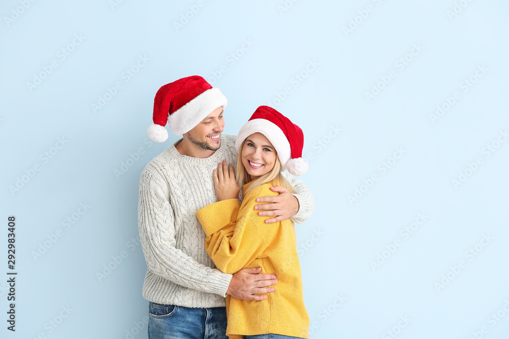 Happy couple in Santa hats on color background Happy couple in Santa hats on color background