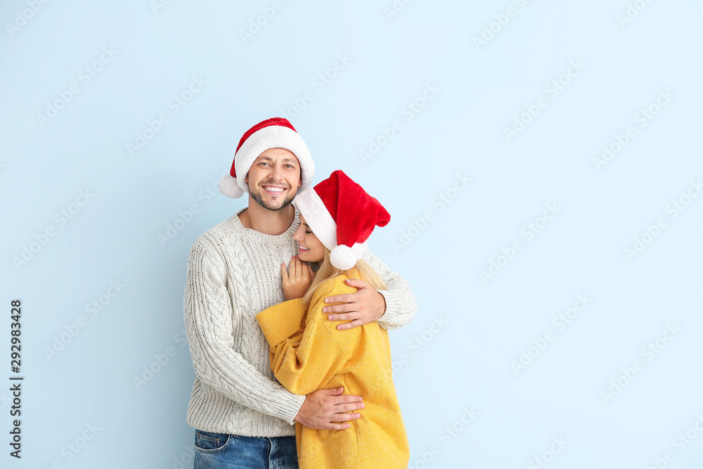 Happy couple in Santa hats on color background Happy couple in Santa hats on color background