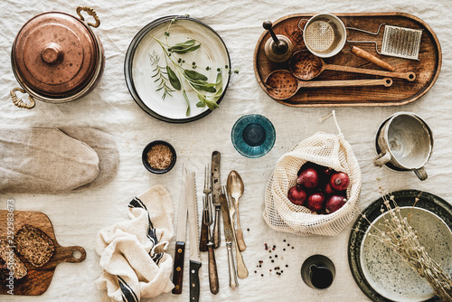 Flat-lay of various kitchen utensils, rustic tablewear, plates, dishes, glasswear, pan, mitten, fresh bread and seasonak red onion over white rustic linen tablecloth background, top view photo