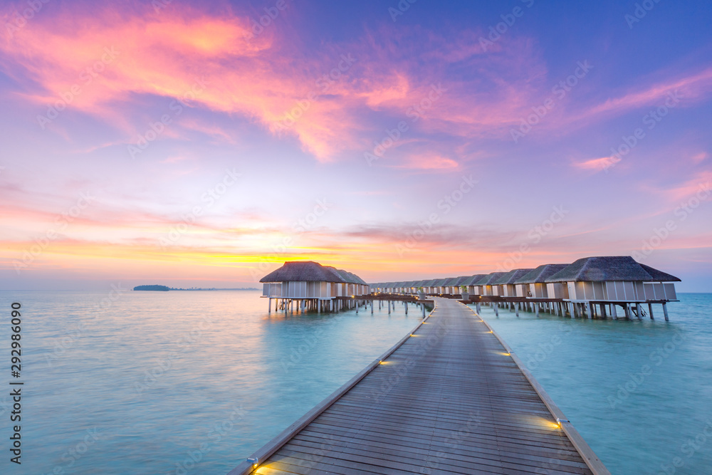 Sunset on Maldives island, luxury water villas resort and wooden pier. Beautiful sky and clouds and beach background for summer vacation holiday and travel concept