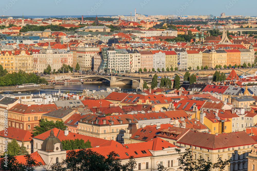 View over the roofs of Prague from the Mala Strana viewpoint with the Vltava river and roads, bridge and dancing house on the shore in sunny day and blue sky