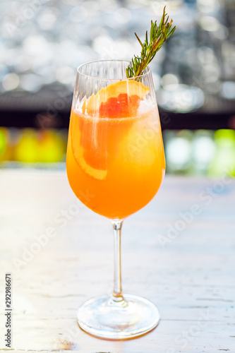 Close-up glass of cocktail decorated with grapefruit and rosemary outdoors.