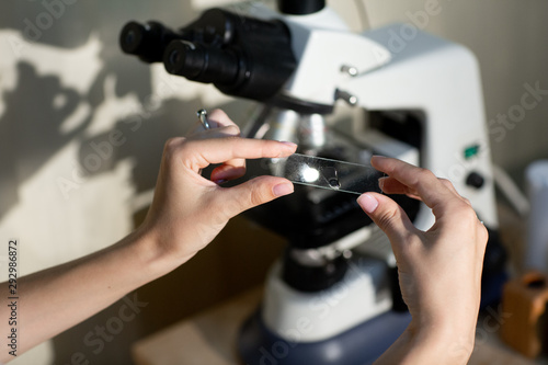 Close up of female hands in white medical uniform, hold a piece of glass with sample analysis. Tests, health check photo