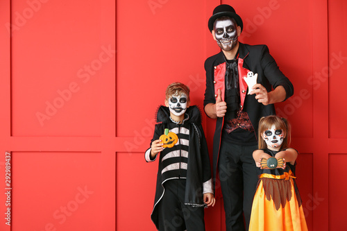 Father with children in Halloween costumes and with cookies on color background