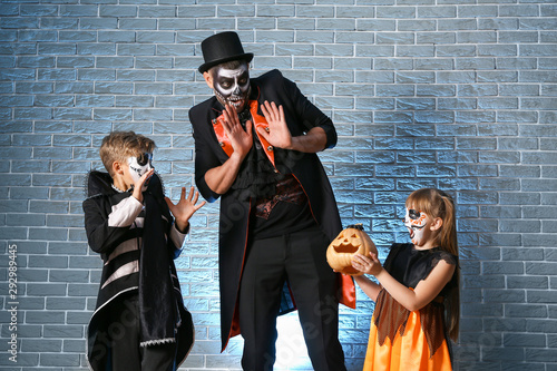 Father with children in Halloween costumes and with pumpkin on brick background