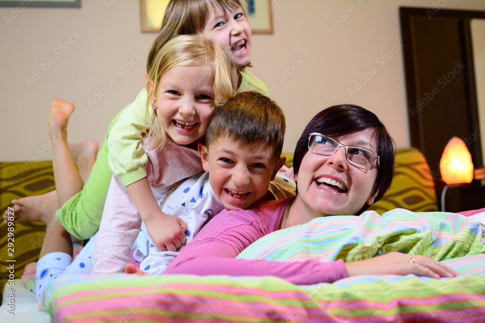 Mother enjoys playing with her children in the morning after sleeping comfortably at home. A brother and two sisters play joyfully with their mother at the start of a weekend morning