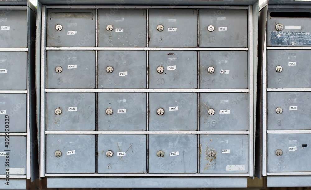 Fototapeta premium Apartment mailboxes lined up in a row. The numbered boxes are metal and appear very worn out with scratches, dirt and other markings.
