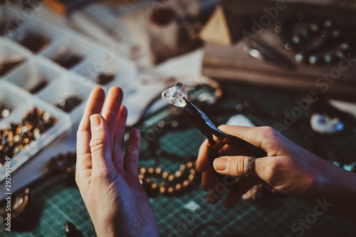 Creative woman is holding pliers and crystal clear quartz in it.