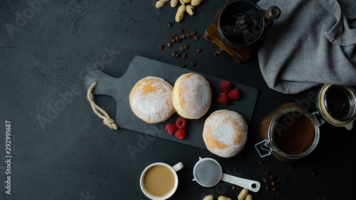 Pączki z cukrem pudrem z malinami i kawą leżące na czarnym tle. Widok z góry.