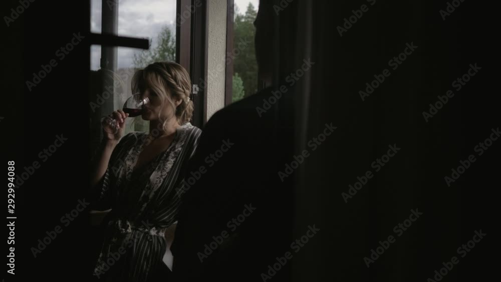 Young beautiful loving couple sitting on the windowsill and drinking wine. The girl drinks wine and looks lovingly at her young man Young beautiful loving couple sitting on the windowsill and drinking wine. The girl drinks wine and looks lovingly at her young man