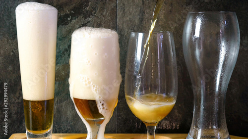 Pouring beer into traditional beer glasses on black slate bar table, beer tasting on wooden paddle.