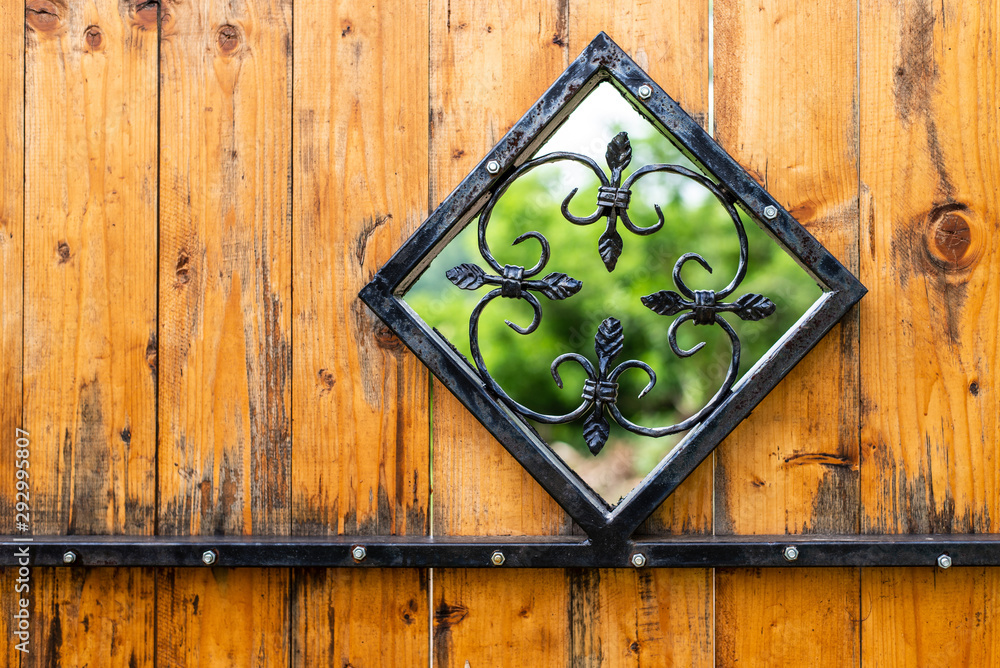 Iron window in rhombus shape with curly ornaments on the wooden door.