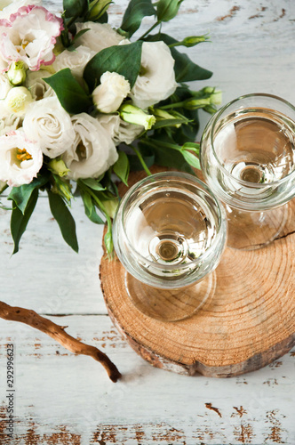 Glasses with wine on a white rustic wooden background with a bouquet of flowers. Wedding table greeting card. Wedding invitation light background.