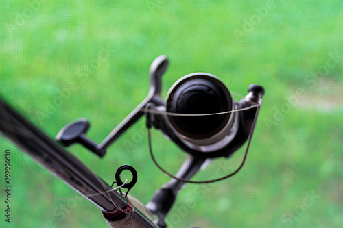 Spinning reel on a green blurred background. Concept: outdoor activities, fishing, outdoor recreation. Selective focus.