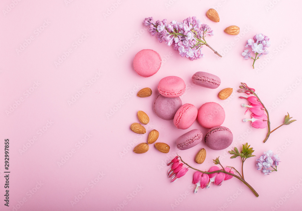 Purple and pink macaron or macaroon cakes with lilac and bleeding heart flowers on pastel pink background.