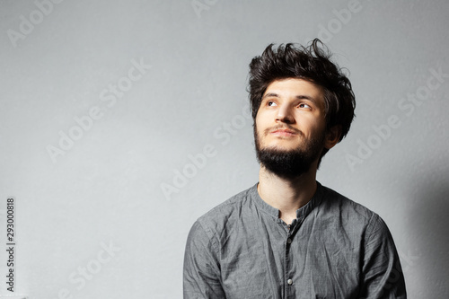 Portrait of pensive young bearded guy with disheveled hair on grey background.