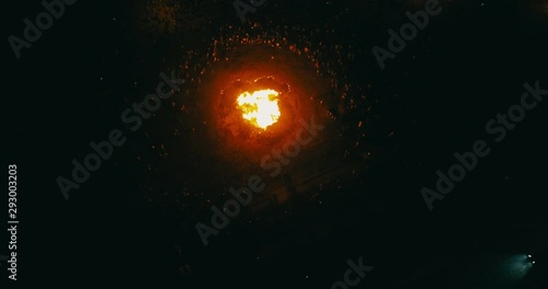 A large crowd of people celebrate near a giant bonfire. Burning hot sparks rise from large fire in the night sky. Belarusian Kupalle. Russian ethnic holiday Ivan Kupala in village. Aerial drone shot. photo