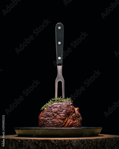 Sous-vide grilled beef steak with fork and herbs on dark background.