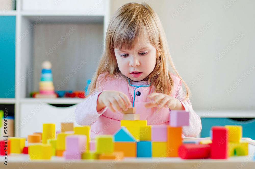 Little girl playing with color wooden blocks sitting at the table Little girl playing with color wooden blocks sitting at the table