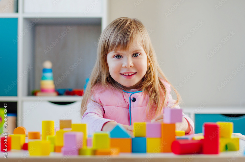 Smiling little girl building toy town with color wooden blocks Smiling little girl building toy town with color wooden blocks