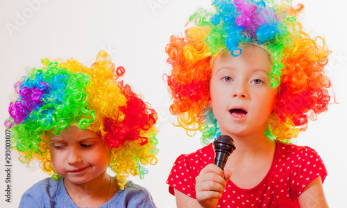 Portrait of little cute caucasian child girls superstars singing with the microphone. Funny facial expression.