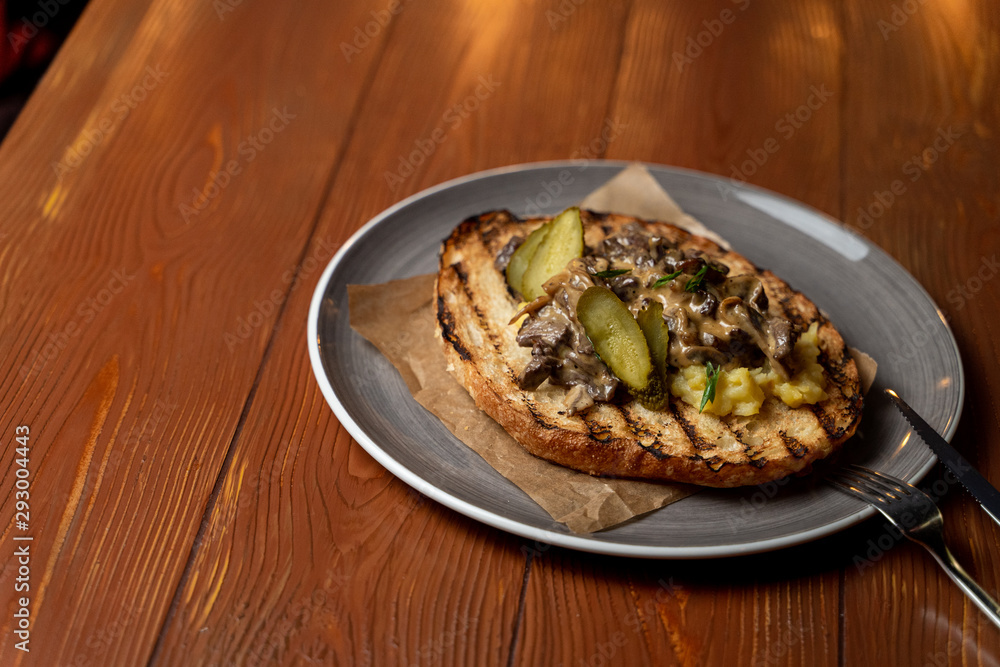 Ciabatta toast with fried button mushrooms, pork and pickled cucumbers on rustic wooden background