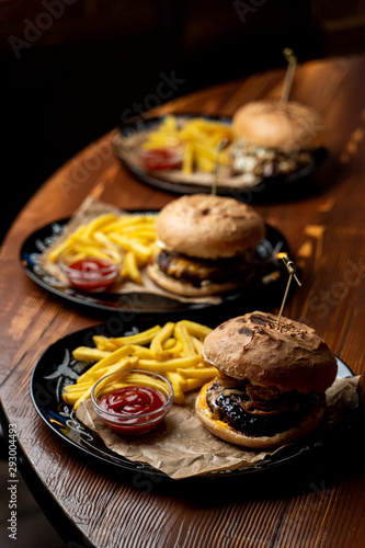 Close up side view of marble beef burgers with cheese sauce and hot french fries on wooden table