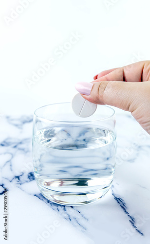 A hand throwing a medicine into a glass quickly dissolves. The effervescent tablets and glass with water