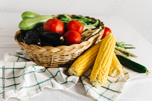 a group of fresh vegetables in a basket  there are tomatoes  zucchini  eggplant  yellow and red bean  cucumber and corn