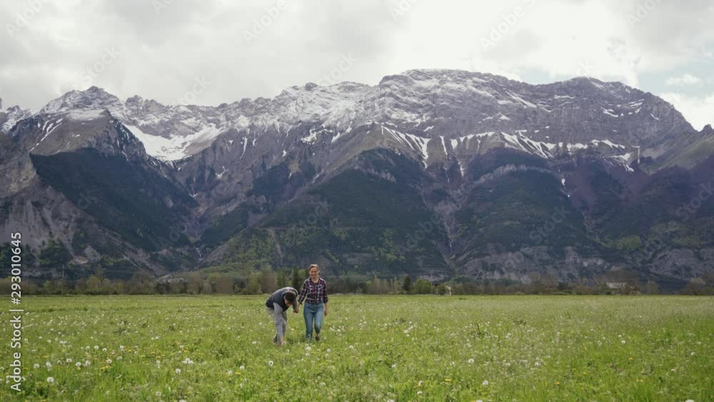 Young happy people holding hands running on dandelion field In mountains. Front view. General plan Young happy people holding hands running on dandelion field In mountains. Front view. General plan