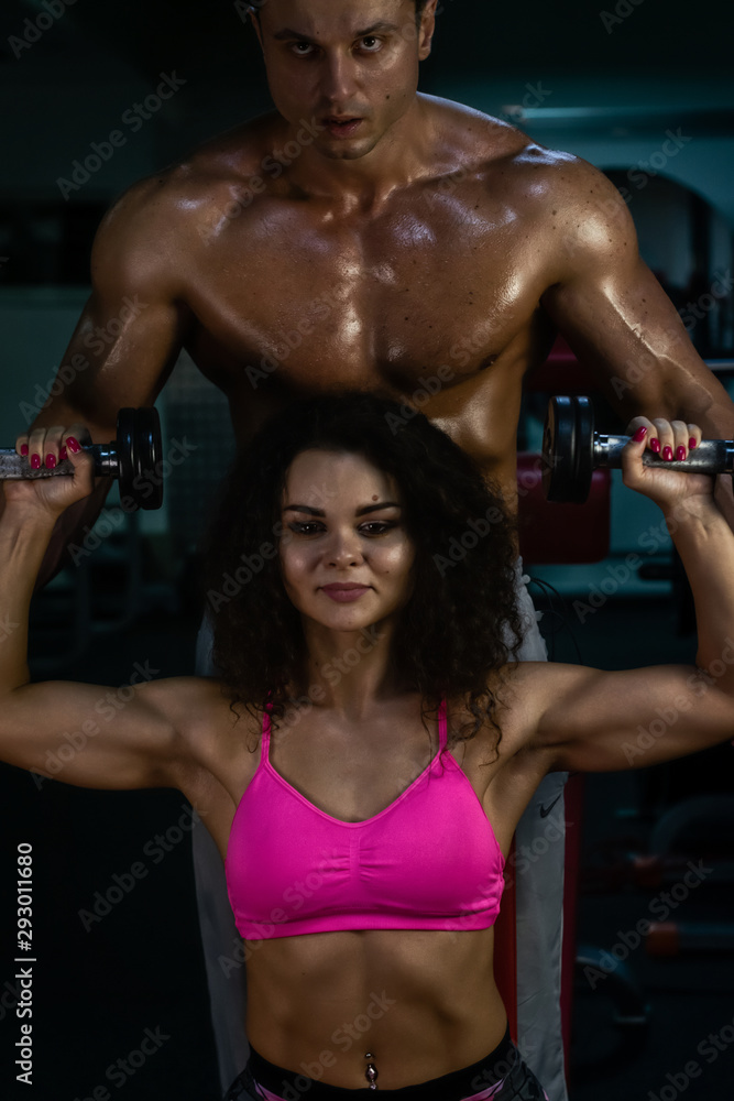 Foto Stock sportive couple in gym . muscular woman and man in gym.sportive  life. fitness. gym. hot curly woman. handsome bodybuilder | Adobe Stock