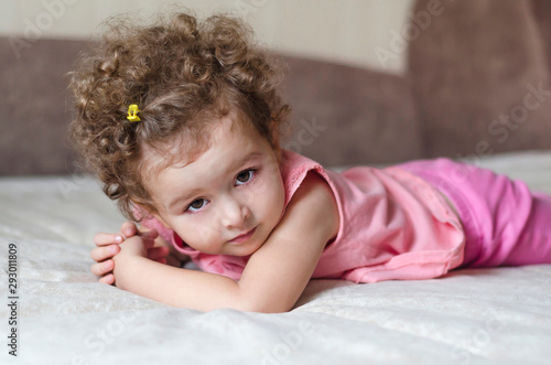 portrait of a little adorable cute girl with curly hair on a pink and grey background. happy childhood. beautiful baby posing and look at the camera.
