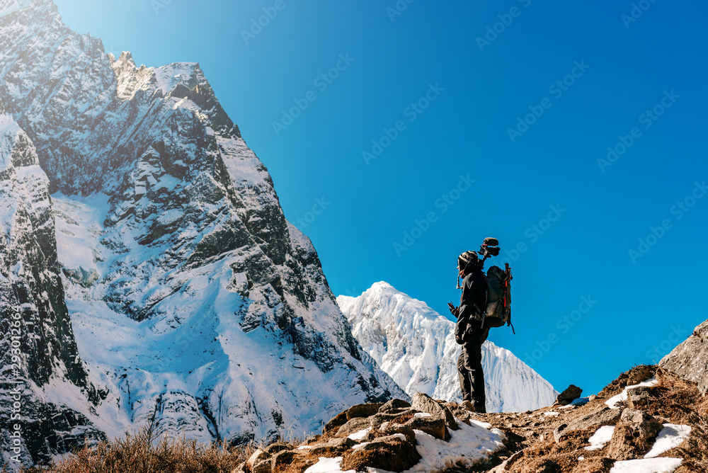 Snow covered mountain peaks and male trekker in Himalayas, Nepal during bright sunny day with blue sky.	