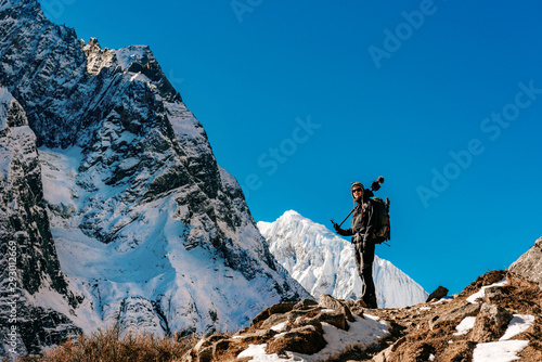 Snow covered mountain peaks and male trekker in Himalayas, Nepal during bright sunny day with blue sky. 