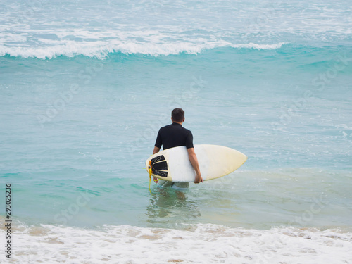 A surfer with a surfboard goes into the ocean, looks into the ocean. Short board. Atlantic Ocean.